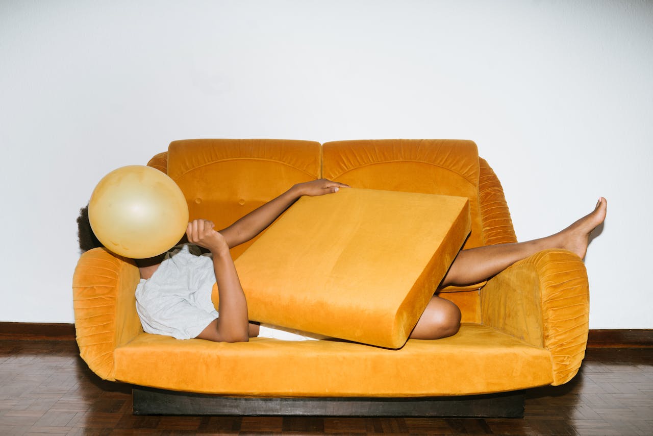 Mastering the First Impression: Your intriguing post title goes here A person lies on a yellow sofa, holding a balloon with a playful, relaxed pose indoors.